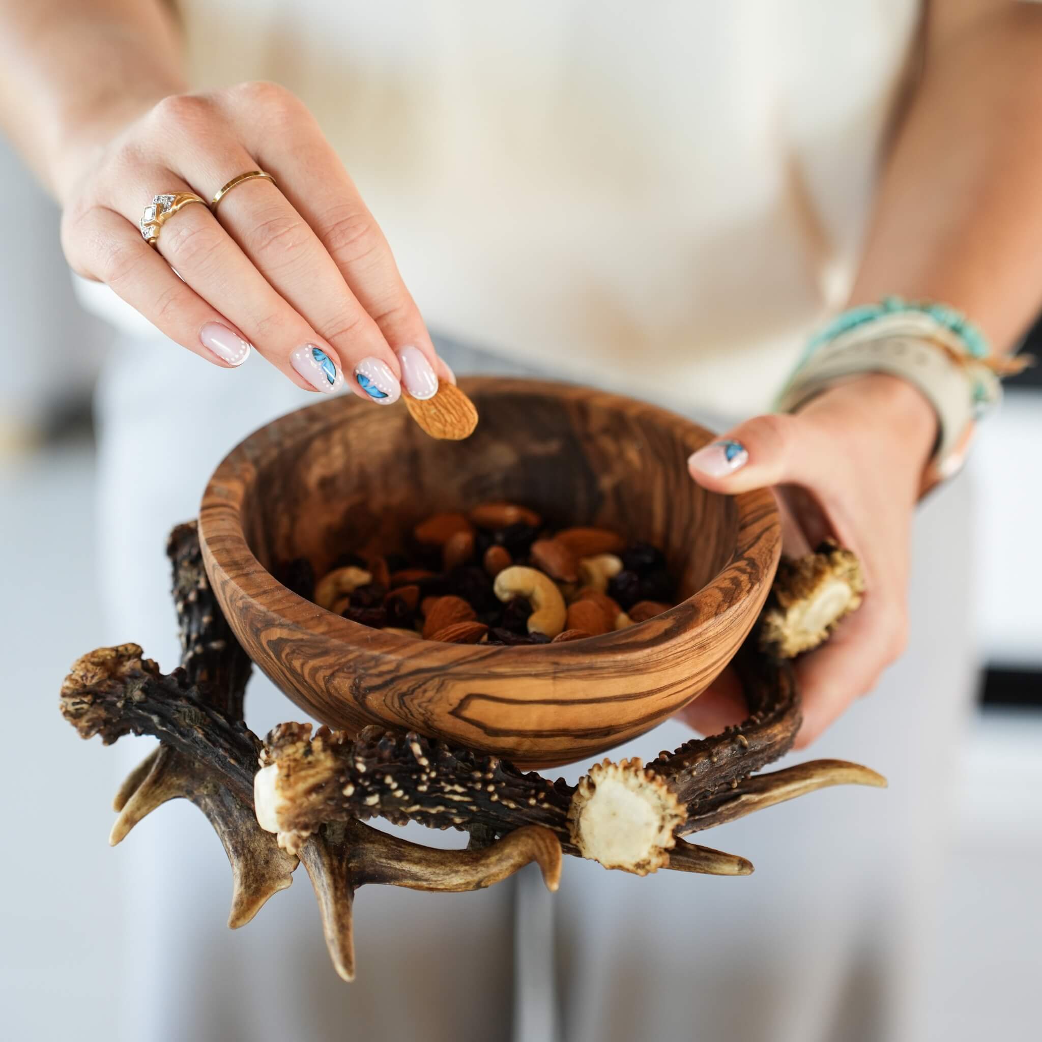 Woman holding a small olive wood bowl with a mix of nuts and fruits, set in a rustic antler base.