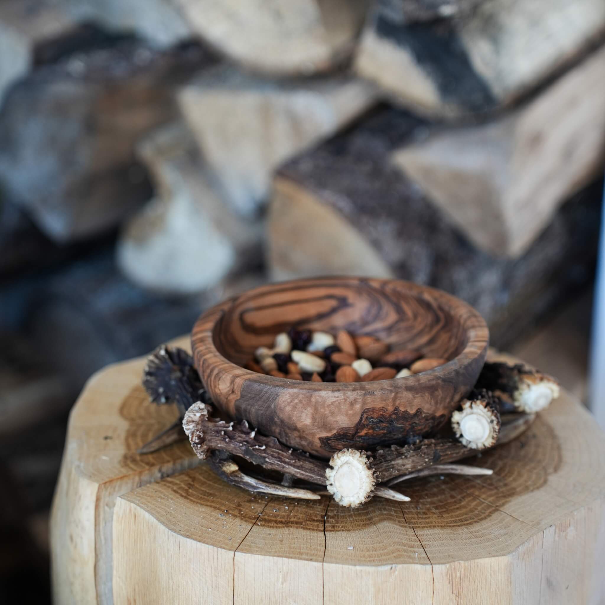 Olive wood bowl with trail mix inside, resting on a log slice and antler frame in a cozy farmhouse setting.