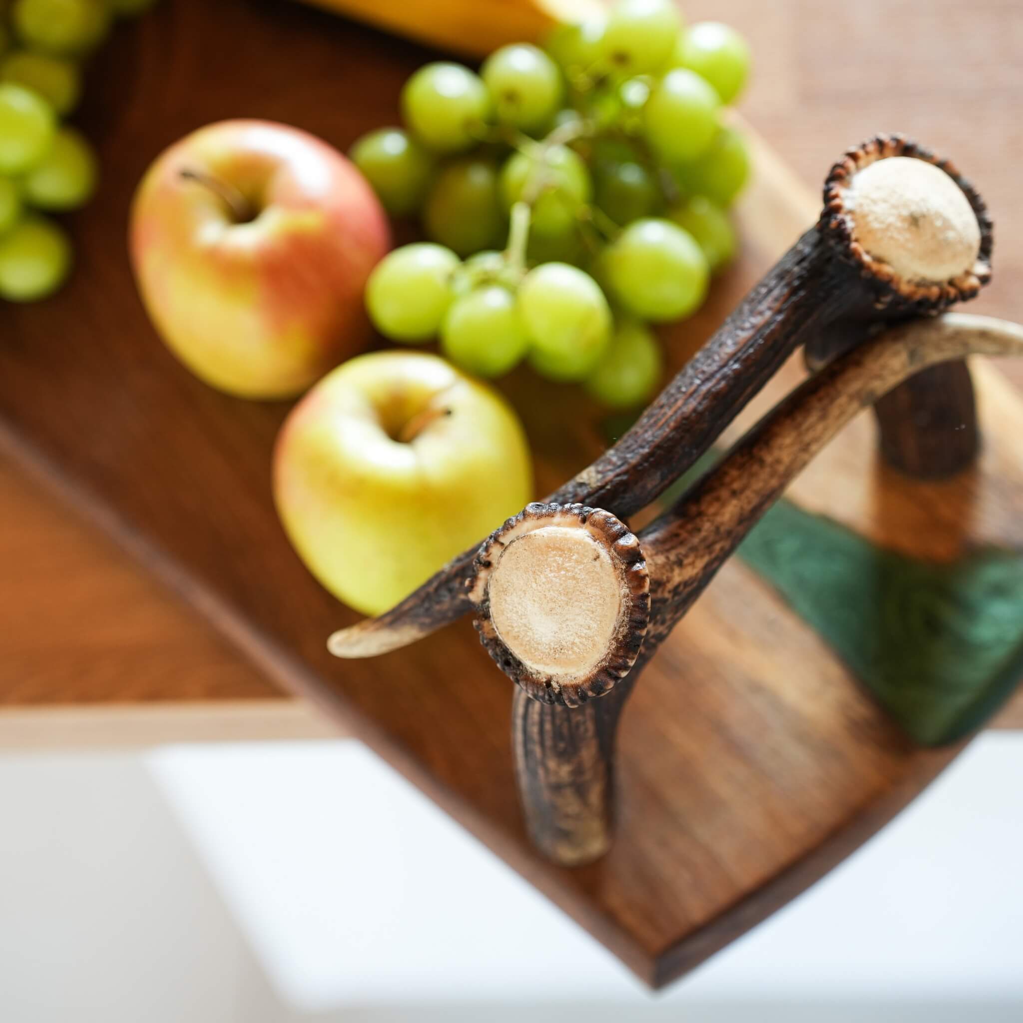 Top view of olive wood tray with real antler handles holding apples, bananas, and grapes.