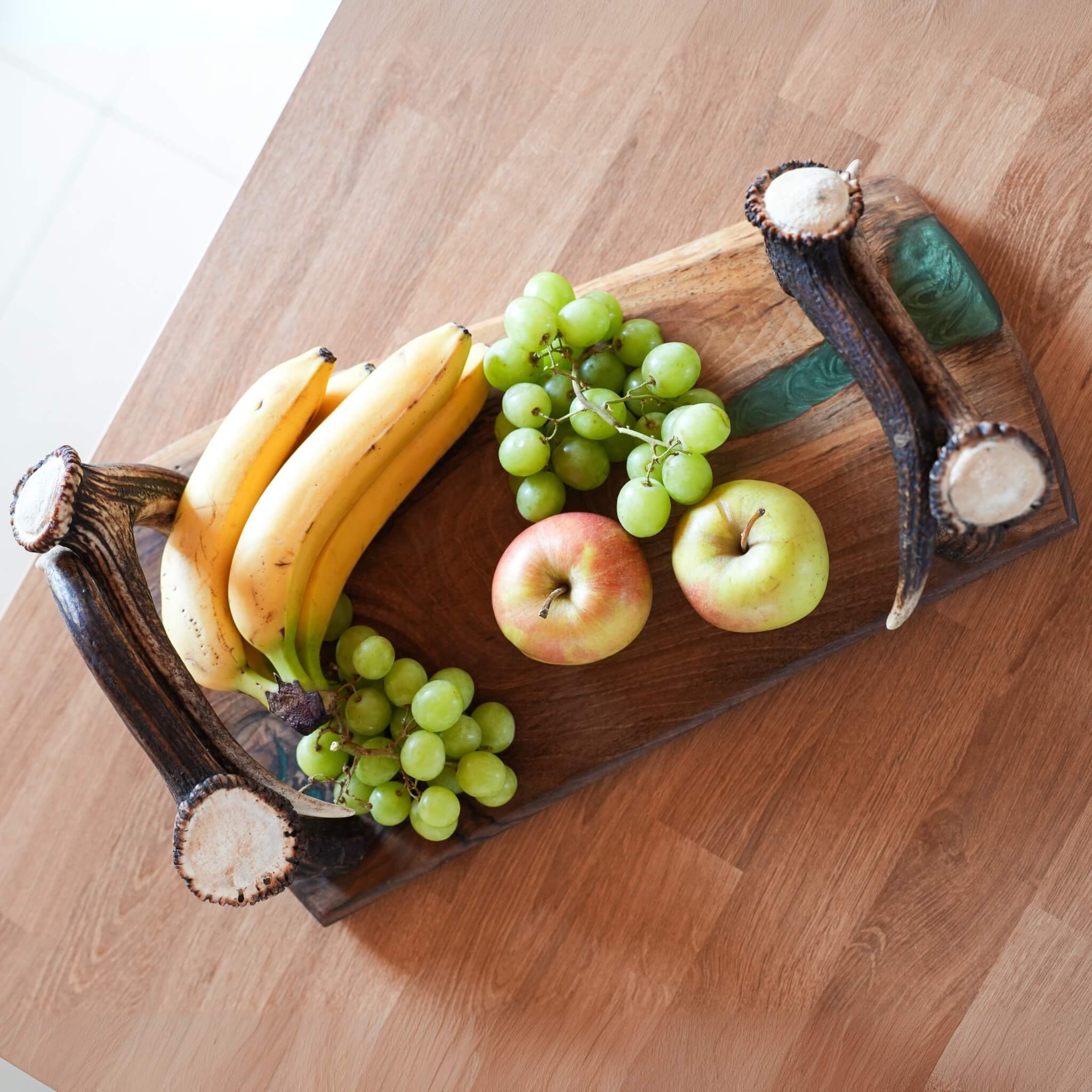 Overhead view of handcrafted olive wood tray with epoxy river and real antler handles, filled with fruits.