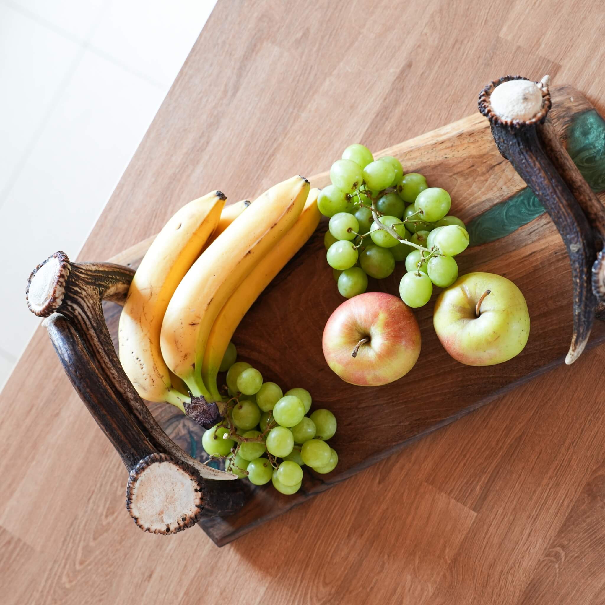 Flat lay of olive wood tray with antler handles, epoxy detail, and fresh fruit display.