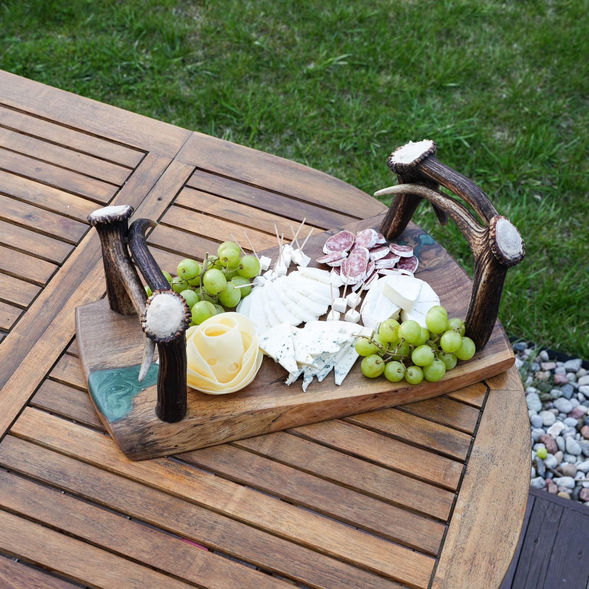 Charcuterie board on rustic olive wood tray with green epoxy resin and real antler handles on outdoor table.