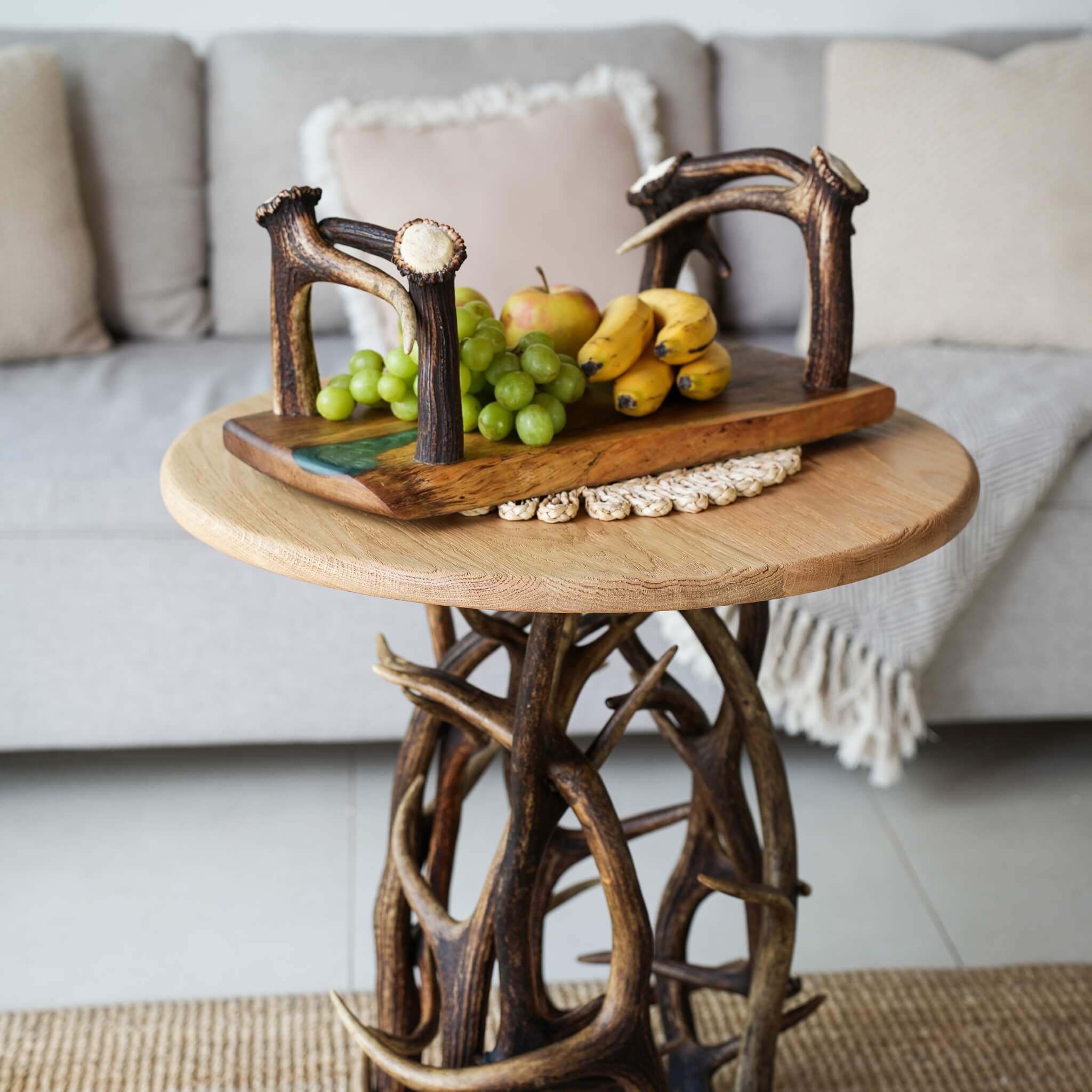 Decorative olive wood tray with antler handles placed on sculptural antler table in living room setting.