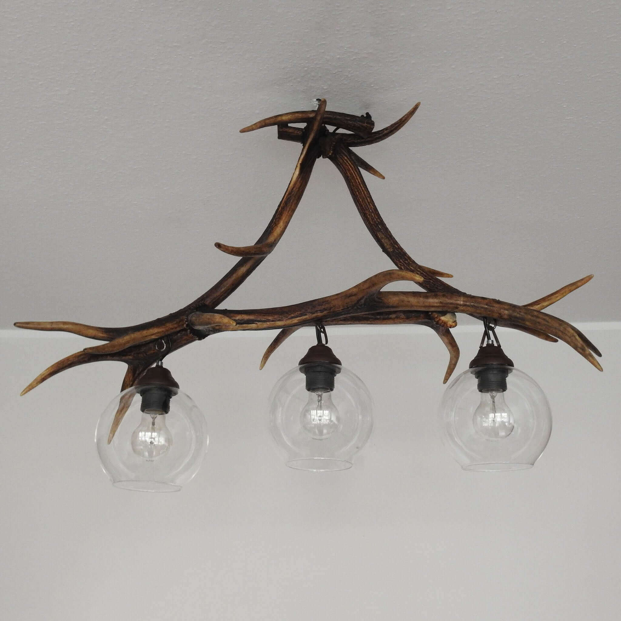 Rustic-inspired pendant lamp featuring authentic red deer antlers, designed to elegantly illuminate any space with its three downward-pointing bulbs.