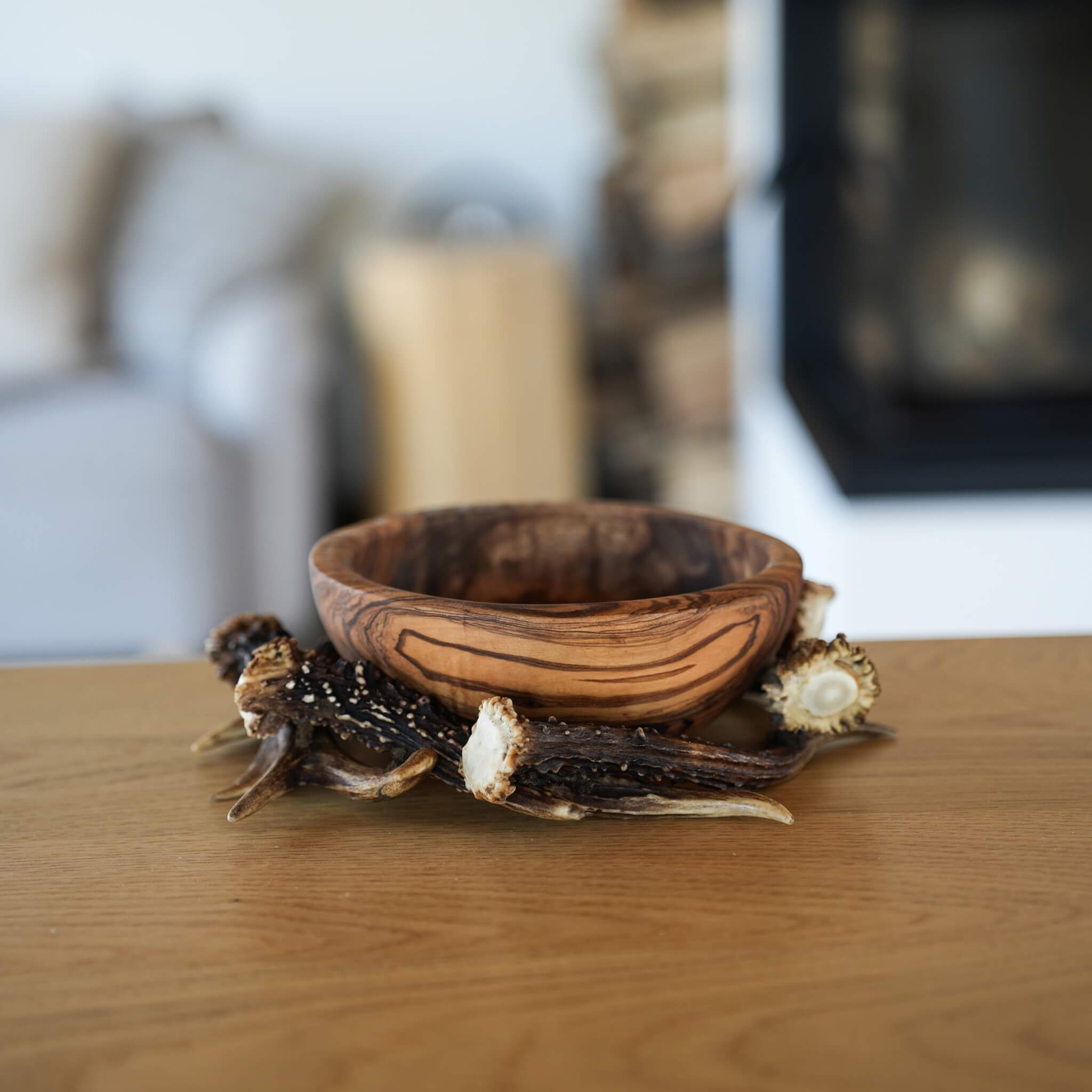 Hand-carved olive wood bowl with natural grain pattern, placed on a table with visible antler decor underneath.