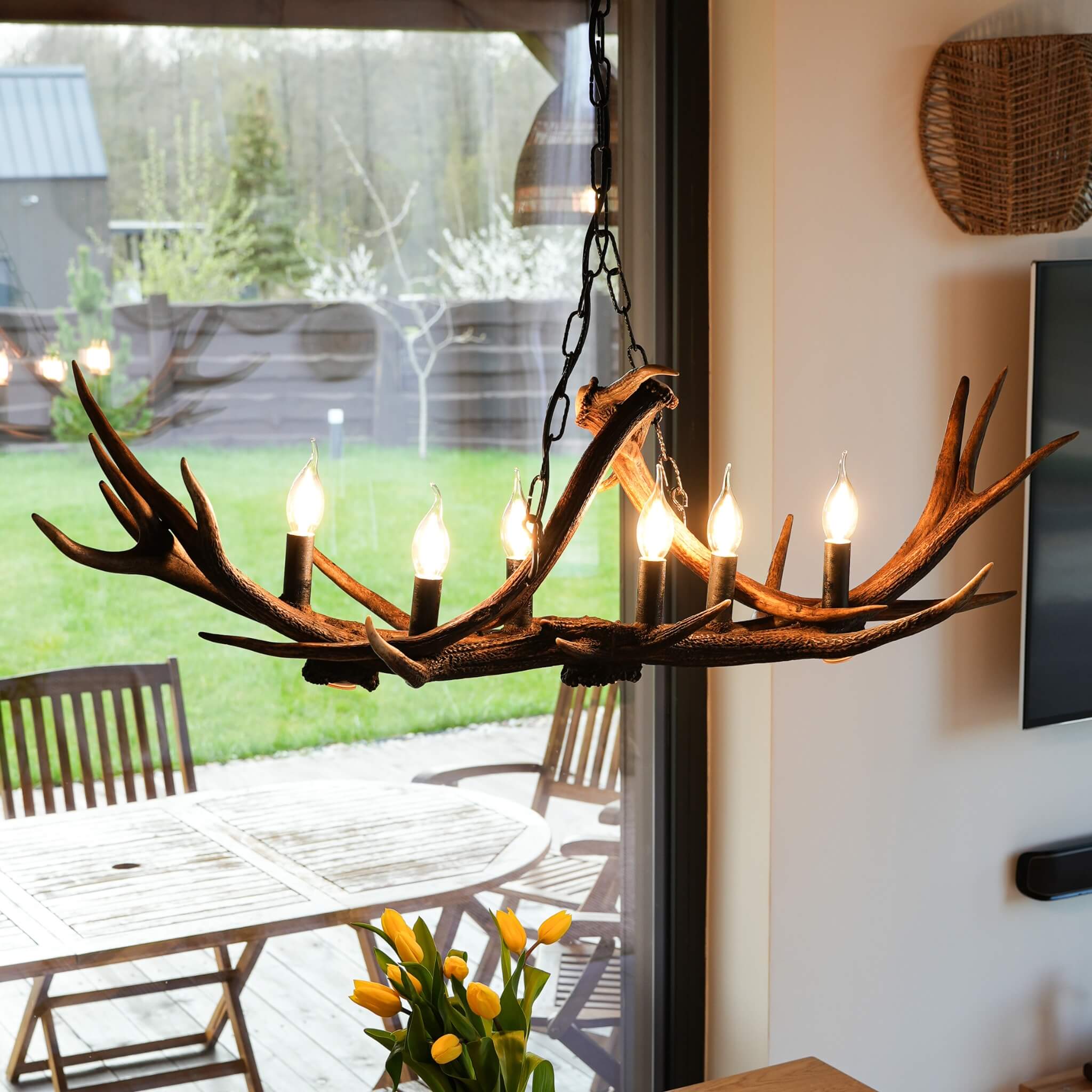 Antler chandelier with candles in dining room room with a glass door leading to an outdoor area.