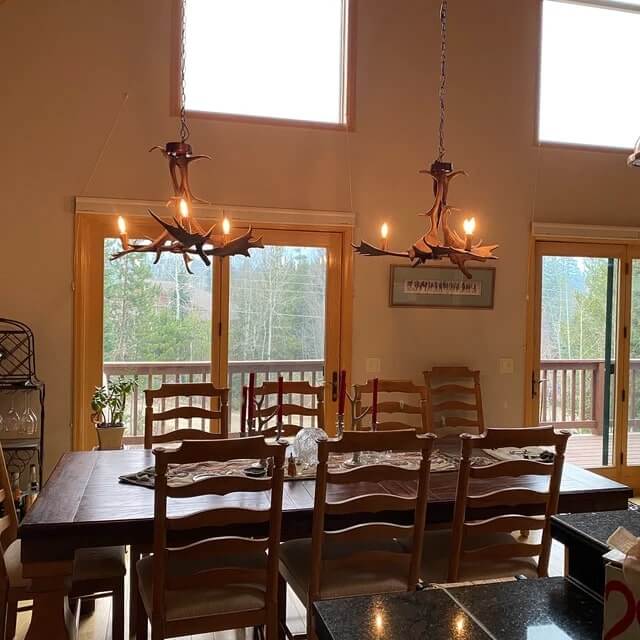 Real antler chandeliers in rustic designed dining room. 2 chandeliers hang over wooden table.