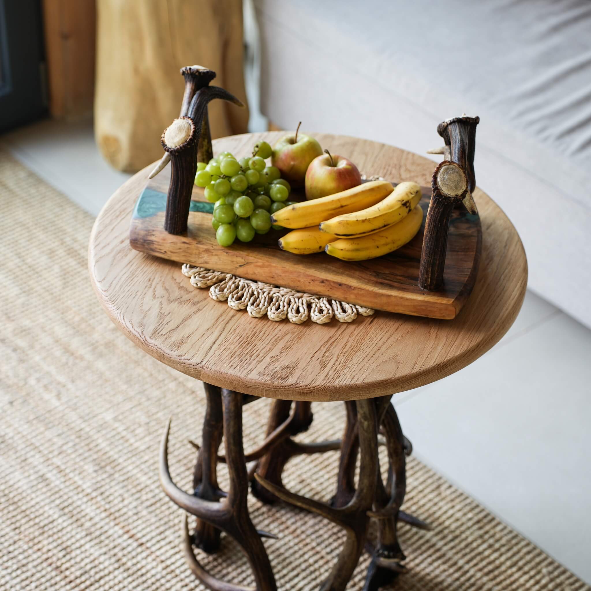 Handmade olive wood serving tray with epoxy resin and antler handles on rustic antler base table in a cozy interior.
