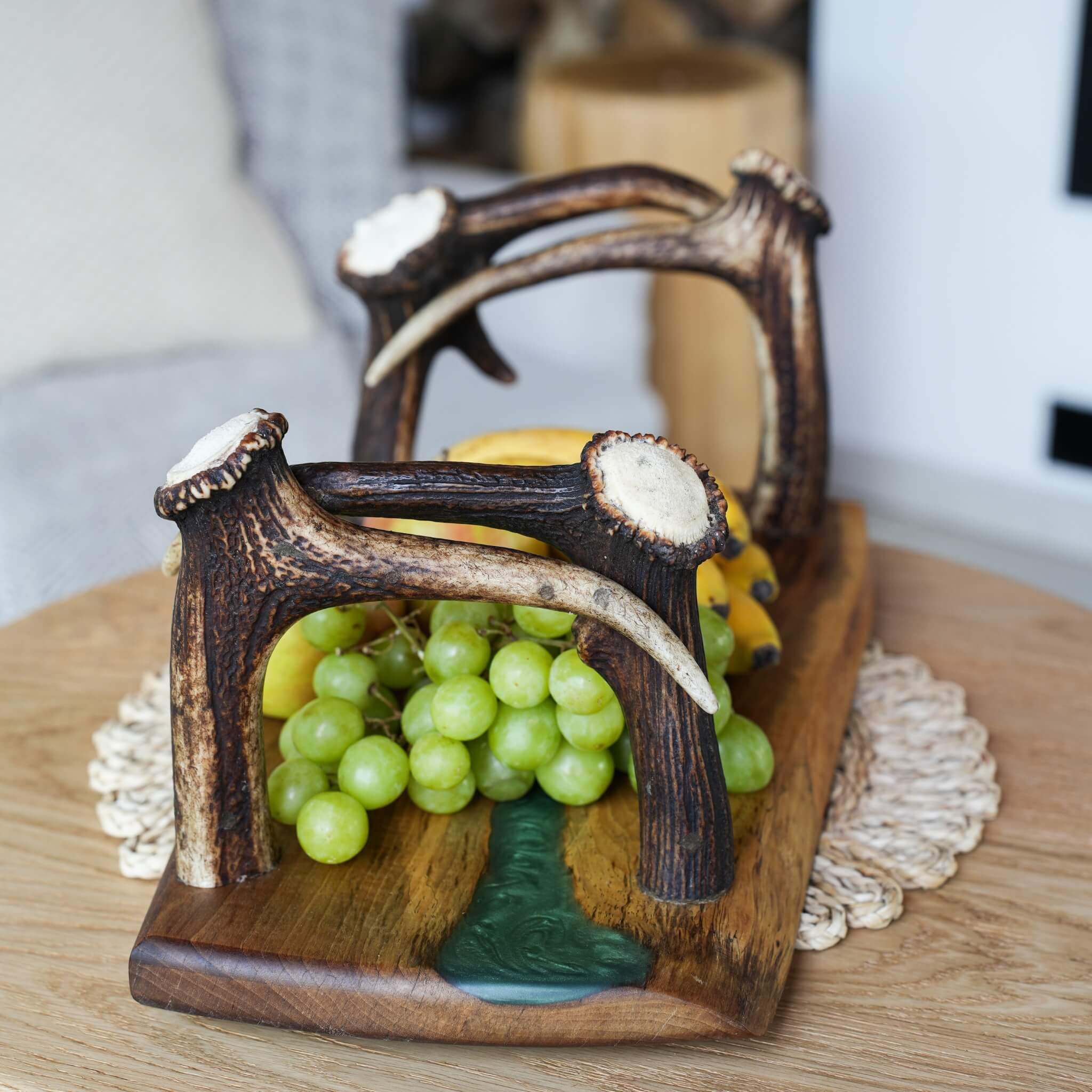 Close-up of antler handle on olive wood serving tray with green epoxy resin detail and fresh fruit.