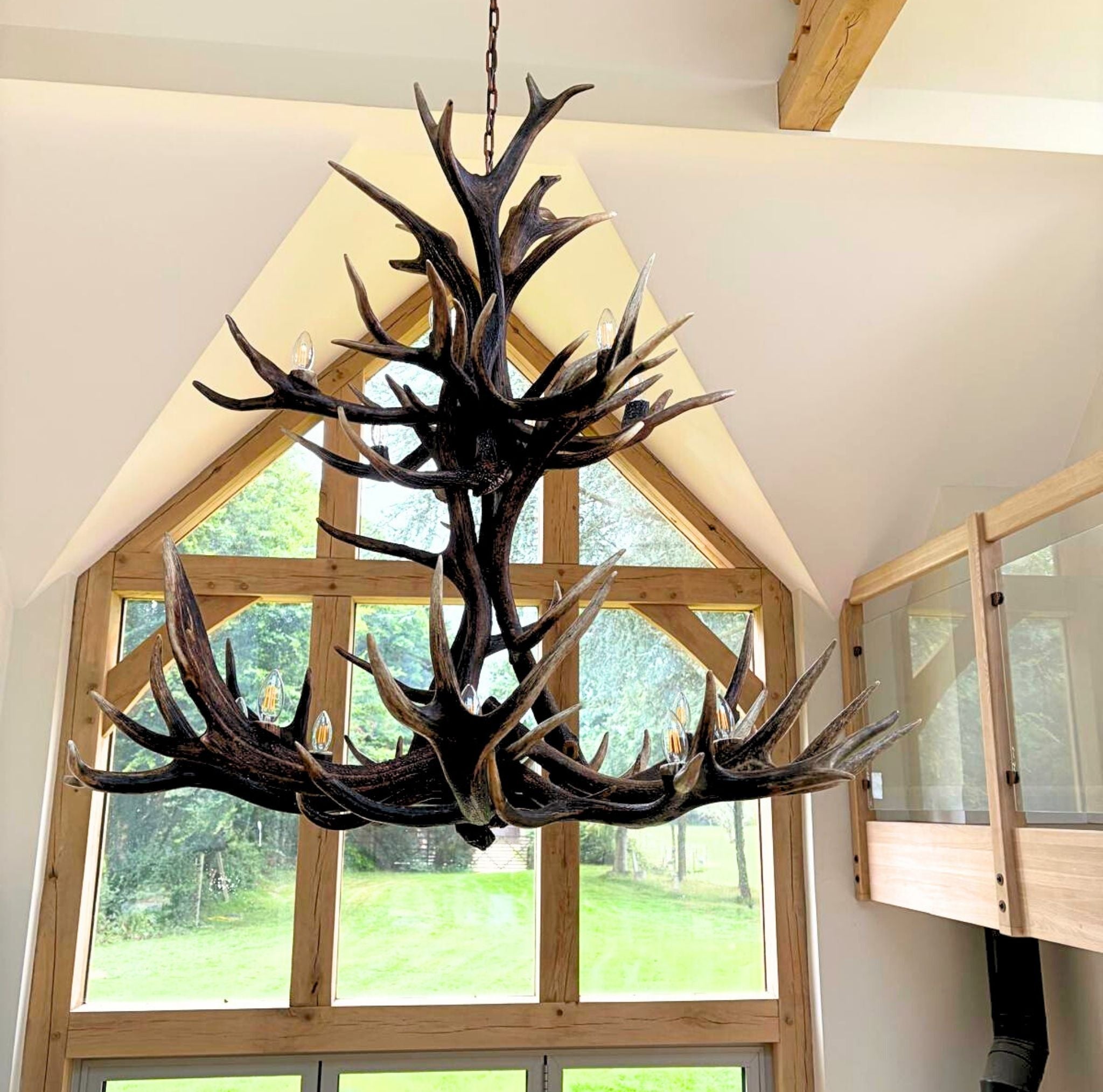 Antler chandelier for 9 lights hanging in a room with large windows.