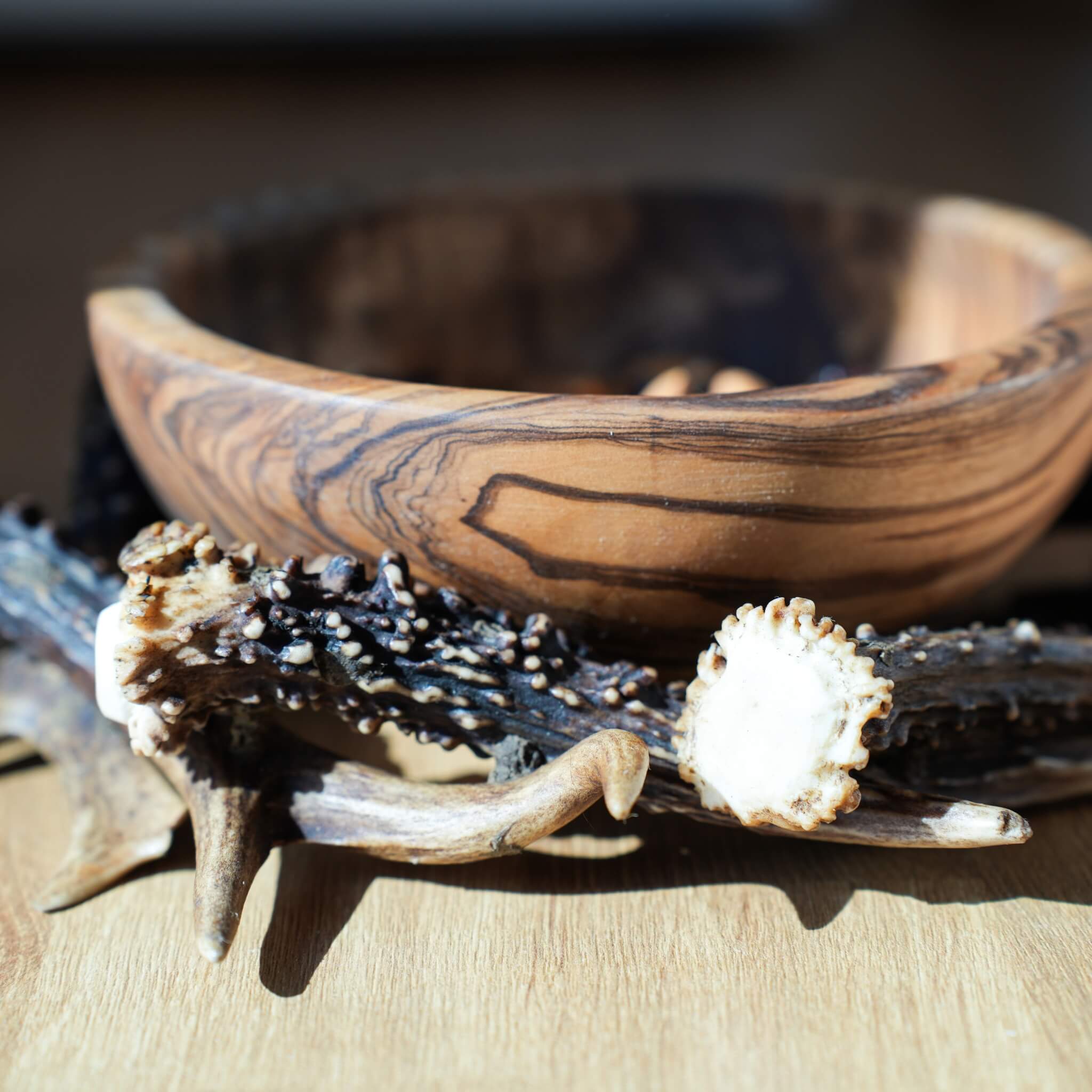 Close-up of a decorative olive wood bowl resting on a circular antler base, displayed on a wooden surface.