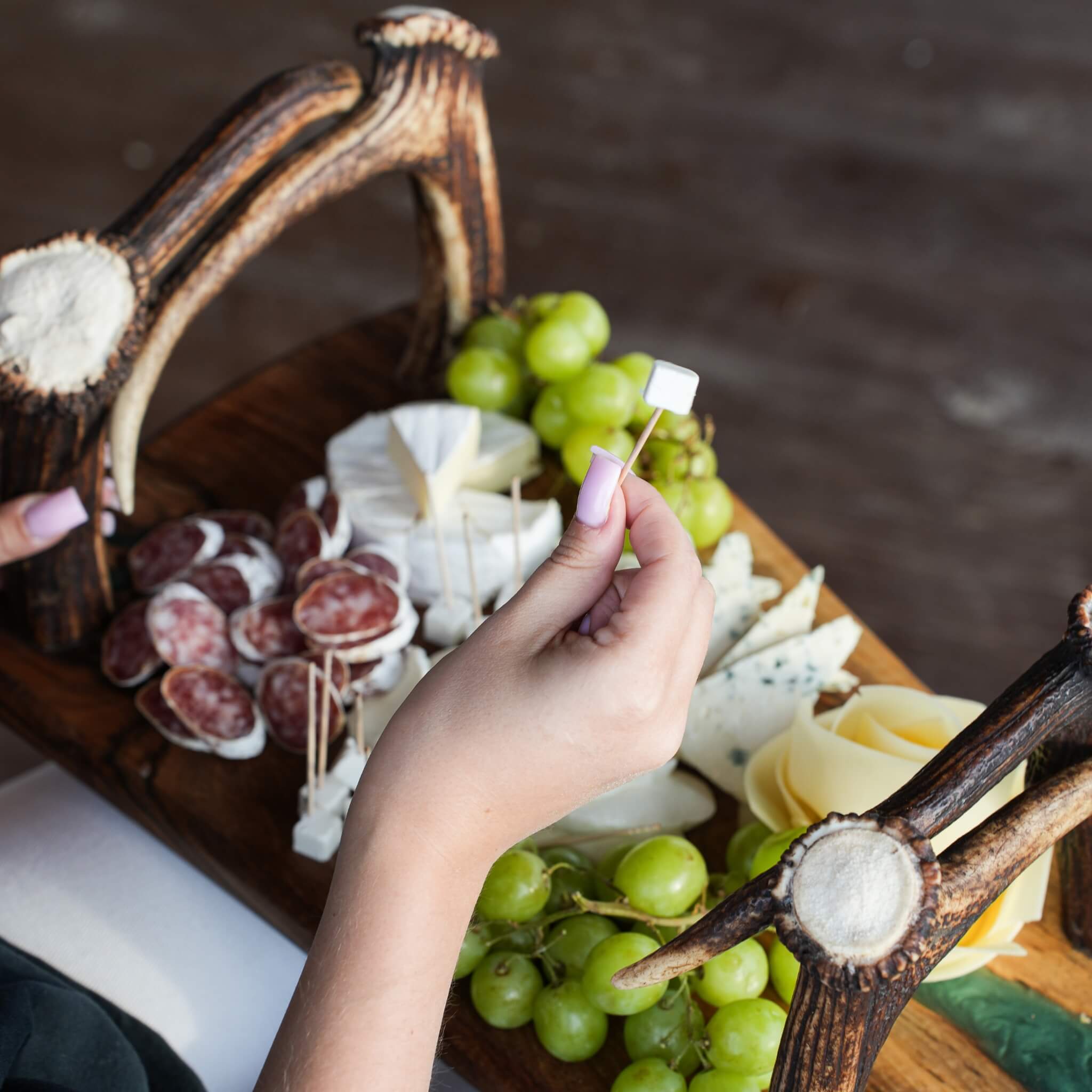 Close-up of a charcuterie board served on olive wood tray with real antler handles, featuring cheese, grapes, and cured meats.