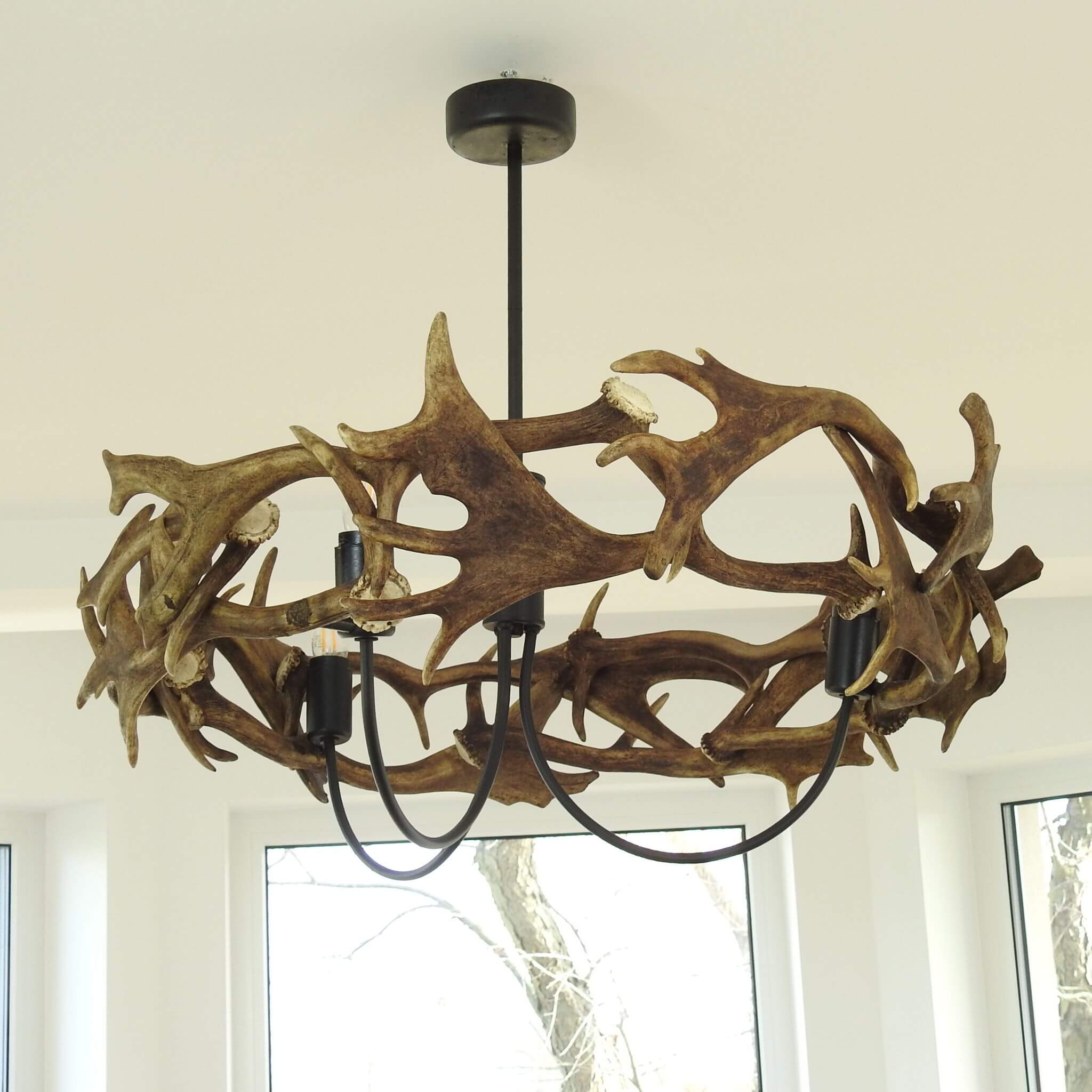 Metal chandeleir with antler ring by the window.